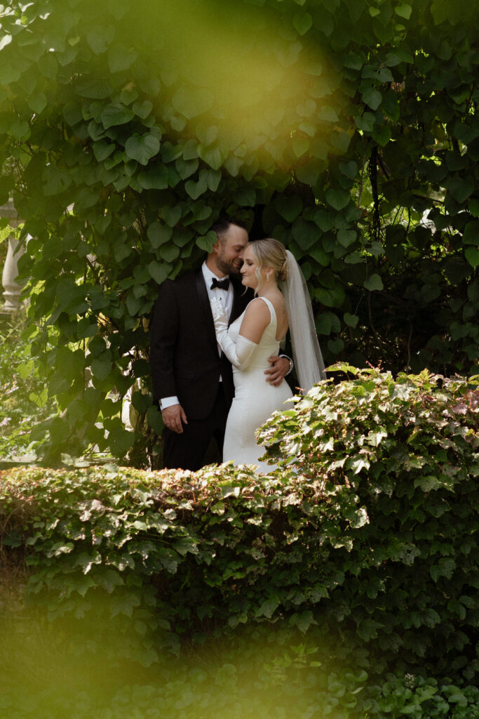 Bride and groom standing in soft light beneath lush greenery at Allan Gardens Conservatory, a year-round portrait spot in Toronto